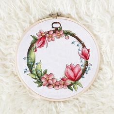 a cross stitch hoop with pink flowers and green leaves on white furnishing, top view