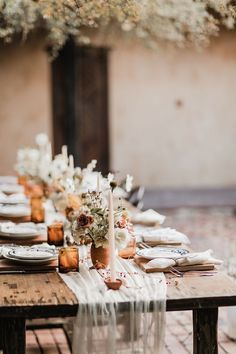 an outdoor table set with place settings and flowers