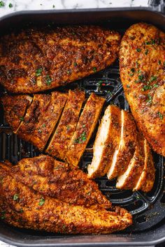 some meat is being cooked in a pan on the grill with tongs and garnishes