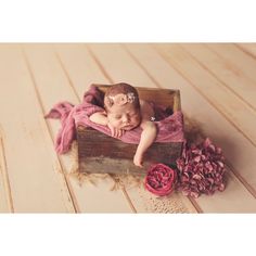 a baby is sleeping in a wooden box with pink flowers on the floor next to it