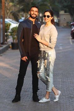 a man and woman standing next to each other on a brick sidewalk with cars in the background