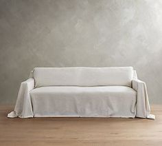 a white couch sitting on top of a hard wood floor next to a gray wall