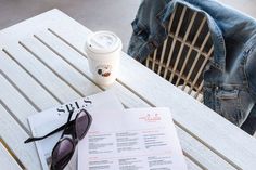 a table with sunglasses, coffee cup and menu on it next to a pair of jeans