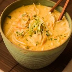 a green bowl filled with soup and chopsticks on top of a wooden mat