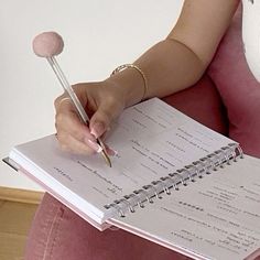 a woman is holding a pen and paper in her hand while sitting on a pink chair