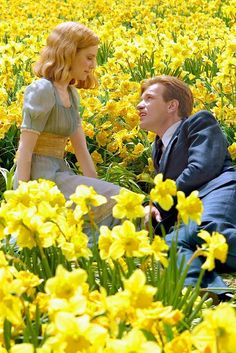 a man and woman sitting in a field of yellow flowers