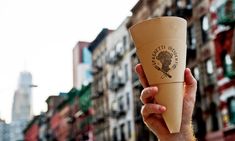 a person holding up a paper cup in front of a city street with tall buildings