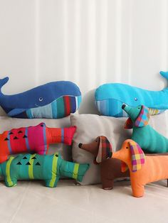 several stuffed animals sitting on top of pillows in the shape of dogs and dolphins, all different colors