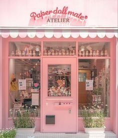 a pink store front with lots of stuff in it's display windows and plants