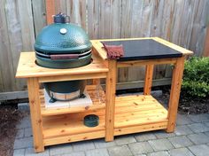 a big green egg sitting on top of a wooden table next to a garden fence