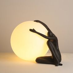 a statue sitting on the ground next to a large ball light that is shaped like a human body