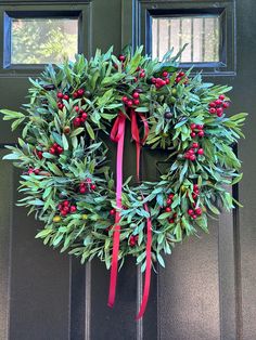 a wreath with red berries and green leaves hanging on the front door's side