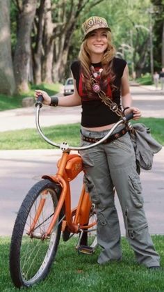 a woman standing next to an orange bike in the grass with her hand on the handlebars