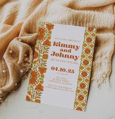 an orange and green wedding card on top of a tan blanket next to a scarf