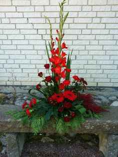 red flowers and greenery sit on a stone bench in front of a brick wall