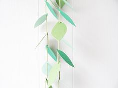 some paper leaves hanging from a string on a white wall with a plant in the middle