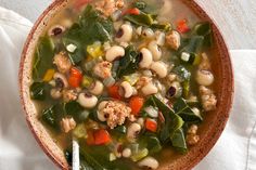 a bowl filled with soup and vegetables on top of a white cloth next to a spoon