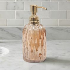 a pink glass soap dispenser sitting on top of a white marble counter