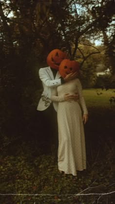 two people dressed up as pumpkins standing in the woods with their heads on each other's shoulders