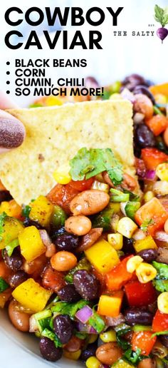 a hand holding a tortilla chip with black beans, corn, and avocado