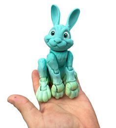 a hand holding a small blue toy rabbit