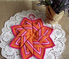 an orange and pink crocheted doily on a white doily next to a vase with purple flowers