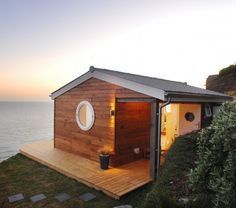 a small wooden house sitting on top of a lush green hillside next to the ocean