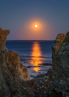 the sun is setting over the ocean as seen through some rocks