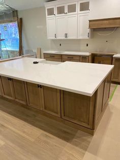 an empty kitchen with white counter tops and wooden cabinets in front of a large window