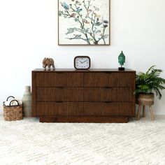 a wooden dresser sitting in front of a painting on the wall next to a potted plant