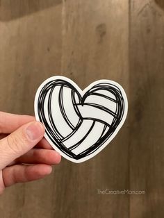 a hand holding up a sticker with a heart in the shape of a volleyball ball