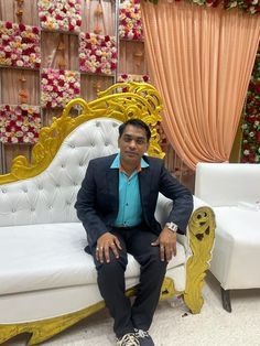 a man sitting on top of a white couch in front of a flower covered wall