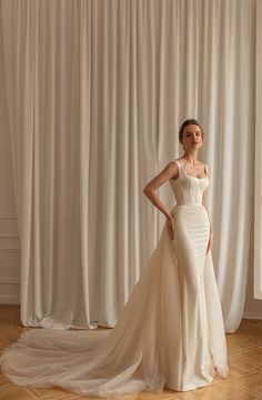 a woman standing in front of a white curtain wearing a wedding dress with an open back