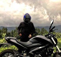 a man standing next to a motorcycle on top of a lush green field under a cloudy sky