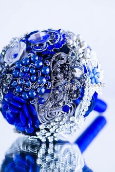 a bridal bouquet with blue beads and jewels on it's head is sitting on a reflective surface