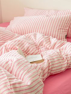 a bed with pink and white striped comforter next to a book on the pillow