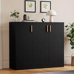 a black cabinet with gold handles in a living room area next to a lamp and potted plant