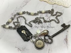 This ONE OF A KIND necklace was made by repurposing an ornate antique key hole plate / escutcheon. The key hole plate has a tiny vintage Bulova watch face peeking through, it even still has the watch hands intact, with a little added glitz of rhinestones. The key hole plate has a beautiful patina that shows its long history.  Dangling below is a vintage beautifully ornate floral handle from a spoon, a long skeleton key, a glass topped "Shift Lock" Royal typewriter key mounted in a smooth edge bezel, a vintage  dimpled glass tear drop pearl with a rhinestone rondelle and faceted Czech glass bead, and finally a mother of pearl heart.    The antiqued silver oval rolo chain is set in an asymmetrical pattern, with round mother of pearl beads that are flanked by rhinestone rondelles, beadcaps an Vintage Keys Decor, Antique Key Necklace, Vintage Bulova Watches, Royal Typewriter, Asymmetrical Pattern, Skeleton Key Necklace, Typewriter Keys, Antique Keys, Pearl Heart