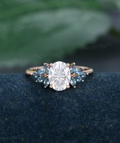 an engagement ring with blue and white stones on it's side, sitting on top of a black cloth