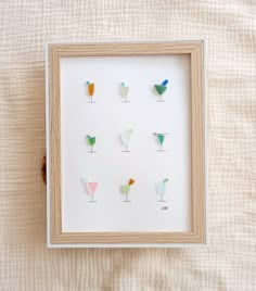 a white frame with several different colored cocktail glasses in it on top of a bed