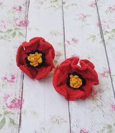 two crocheted red flowers sitting on top of a white table next to each other