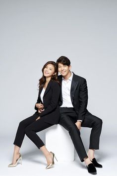 a man and woman sitting on top of a white box posing for the camera with their arms around each other