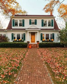 a white house with green shutters and pumpkins on the front lawn in autumn