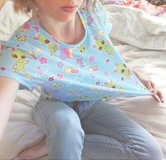 A pastel blue alien shirt featuring little green aliens who are only out to abduct your heart and bring a little shock of pastel to your life. This cropped t-shirt, which has a slightly silky, knit feel, also has contrasting rainbows and stars. It's unisex and fits loose, making for a comfy casual addition to your fairy kei and decora wardrobe while being low-key. Apparel and bedding ship separate from handmade items. Delivered in 2-4 weeks. The colors print more pastel than the items I make mys Playful Green Tops For Sleepover, Playful Light Blue Tops For Loungewear, Playful Short Sleeve Tops For Pajama Party, Cartoon Print Short Sleeve Tops For Pajama Party, Cute Crew Neck Tops For Pajama Party, Cute Short Sleeve Tops For Bedtime, Light Blue Casual Top For Pajama Party, Casual Light Blue Tops For Pajama Party, Stretch Short Sleeve Tops For Sleepover