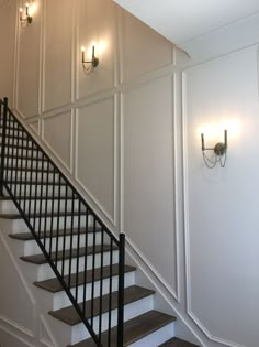 a stair case next to a wall with two lights on it and a chandelier