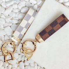 two key chains sitting next to each other on top of white rocks and pebbles in the background