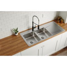 a kitchen sink with two faucets on the counter top and a potted plant next to it