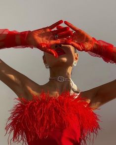 a woman in red is holding her hands up to her head and wearing an orange feathered dress