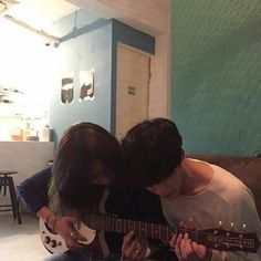 two people are sitting on a couch playing guitar and looking down at the strings that they have attached to their guitars