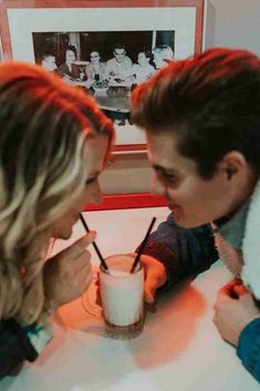 a man and woman sitting at a table with milkshakes in front of them